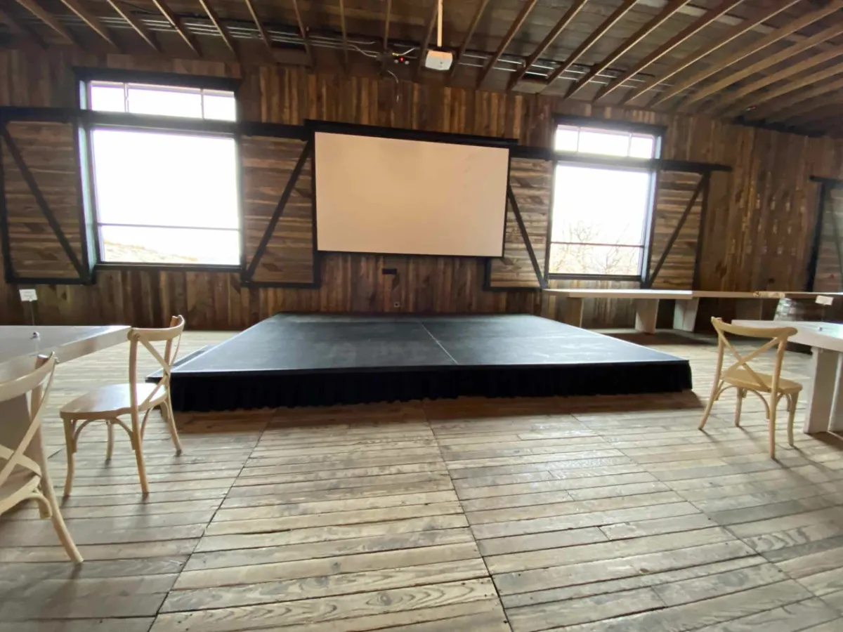 Stage deck below a projection screen between two barn windows