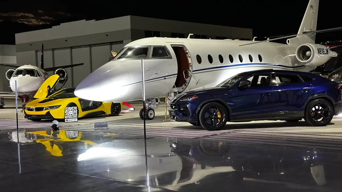 Private jet flanked by a yellow supercar and a blue sedan under event lighting