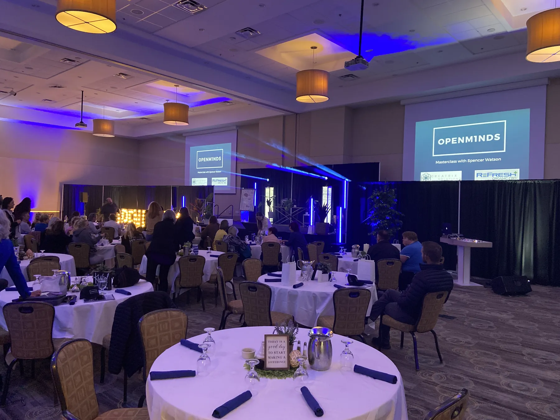 Corporate AV setup in a Utah hotel ballroom with a presentation screen, lectern, and blue wash lighting over banquet rounds