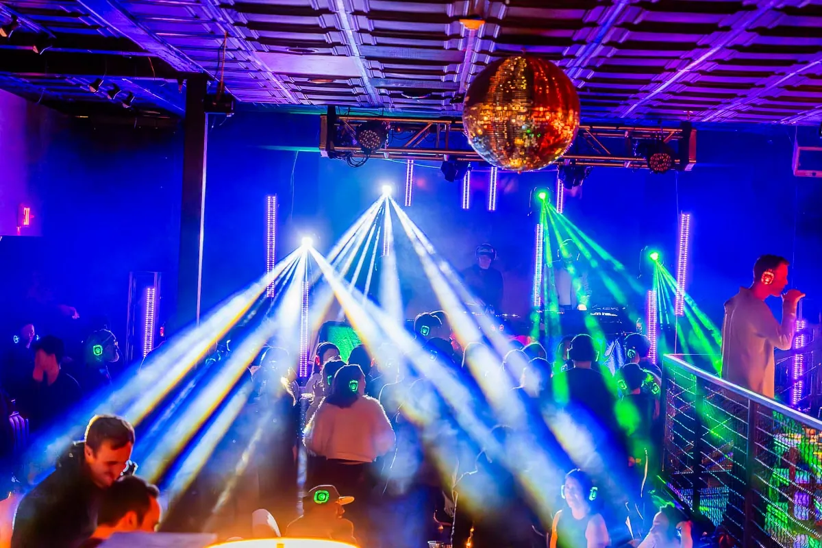 Event lighting with moving head beams and haze cutting across a dance floor under a mirror ball