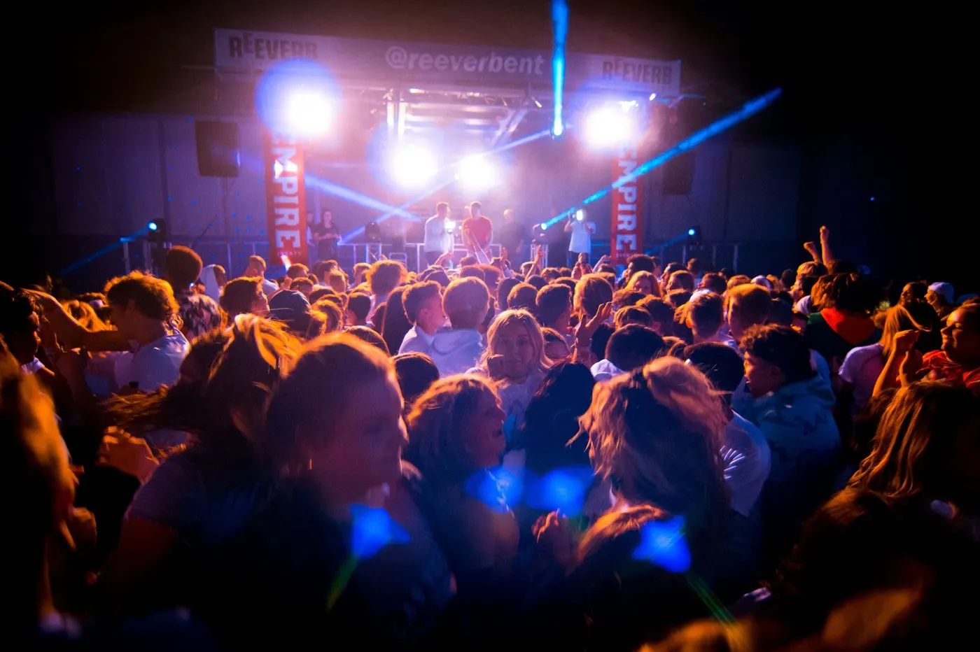 Packed crowd under stage lighting and a PA system at a Reeverb Entertainment event