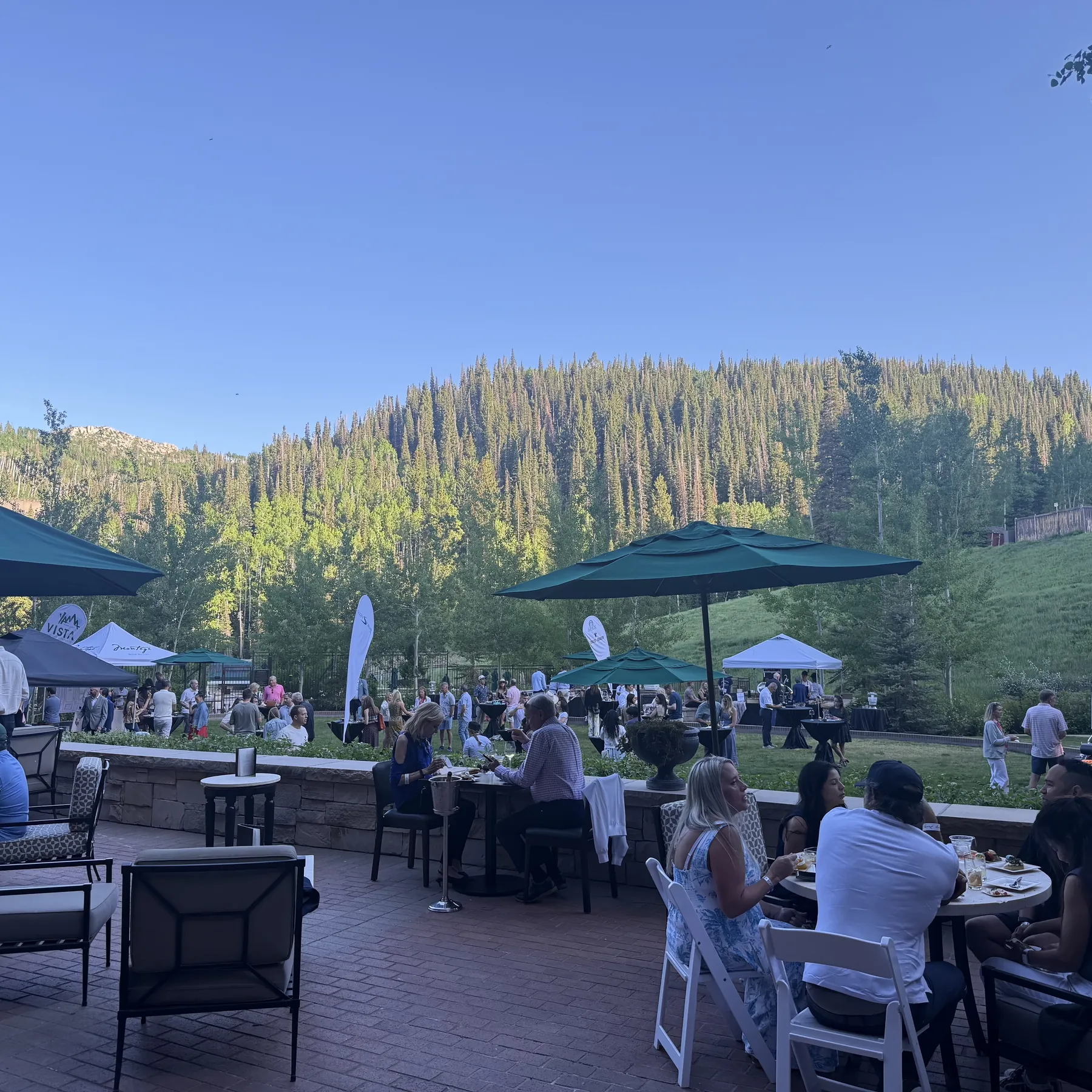 Cocktail hour sound on a mountain resort patio with guests at tables and forested slopes behind
