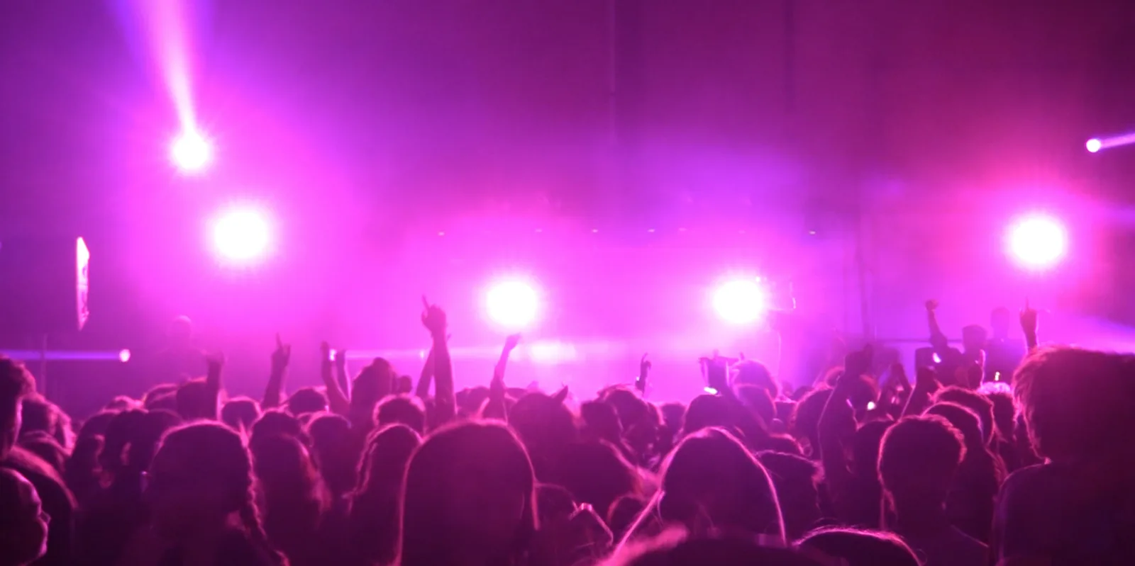 Concert lighting with magenta beams and haze over a crowd with hands raised