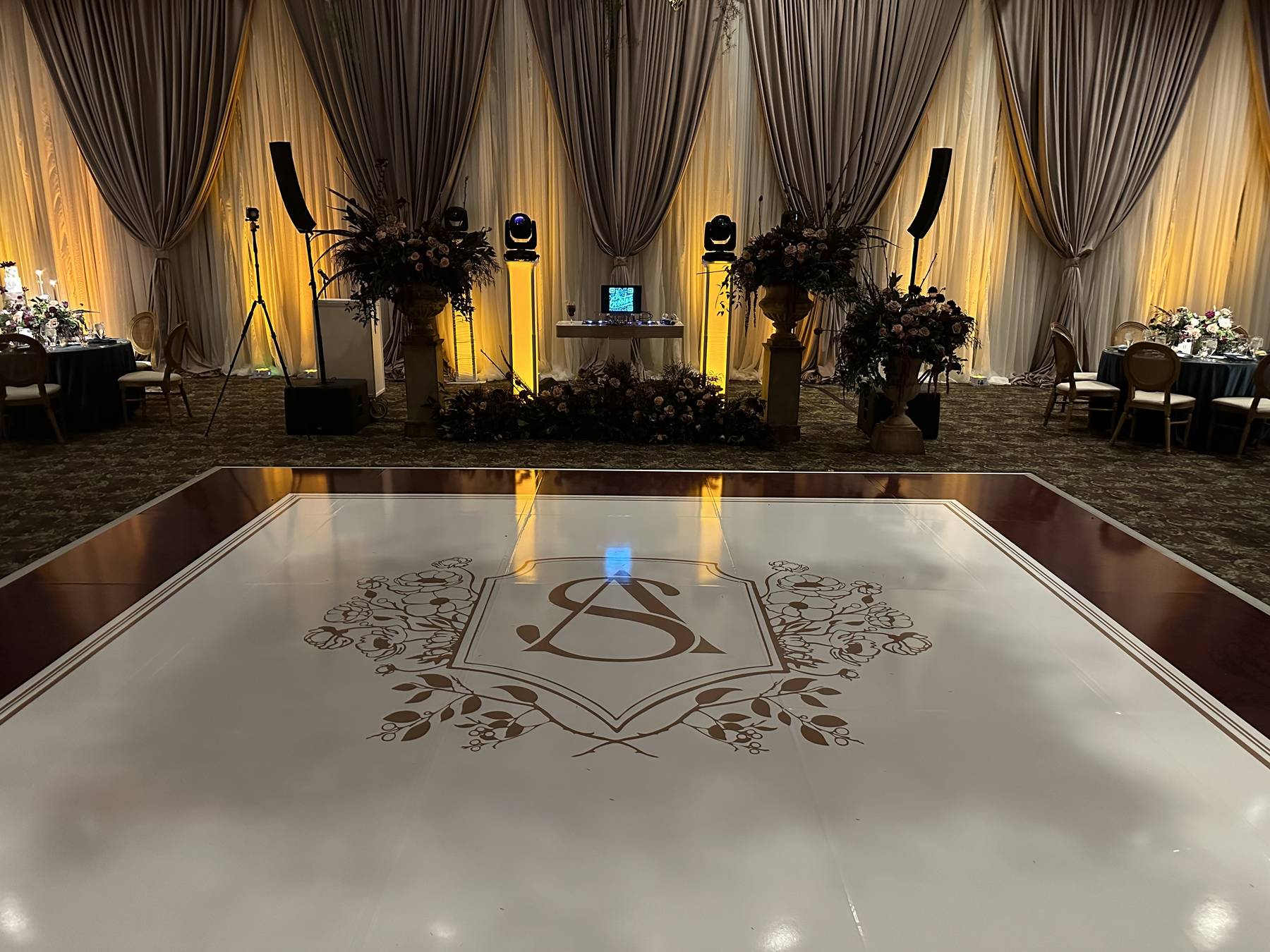 Draped ballroom with monogrammed white dance floor and warm uplighting