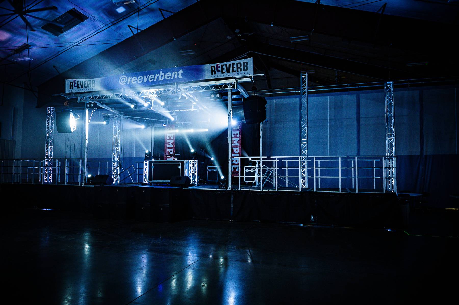 Industrial venue with goalpost truss stage, haze, and blue beams